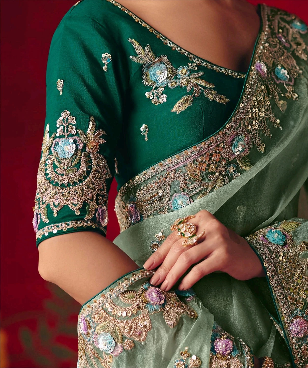 Green saree with intricate gold and multicolor embroidery on a red background